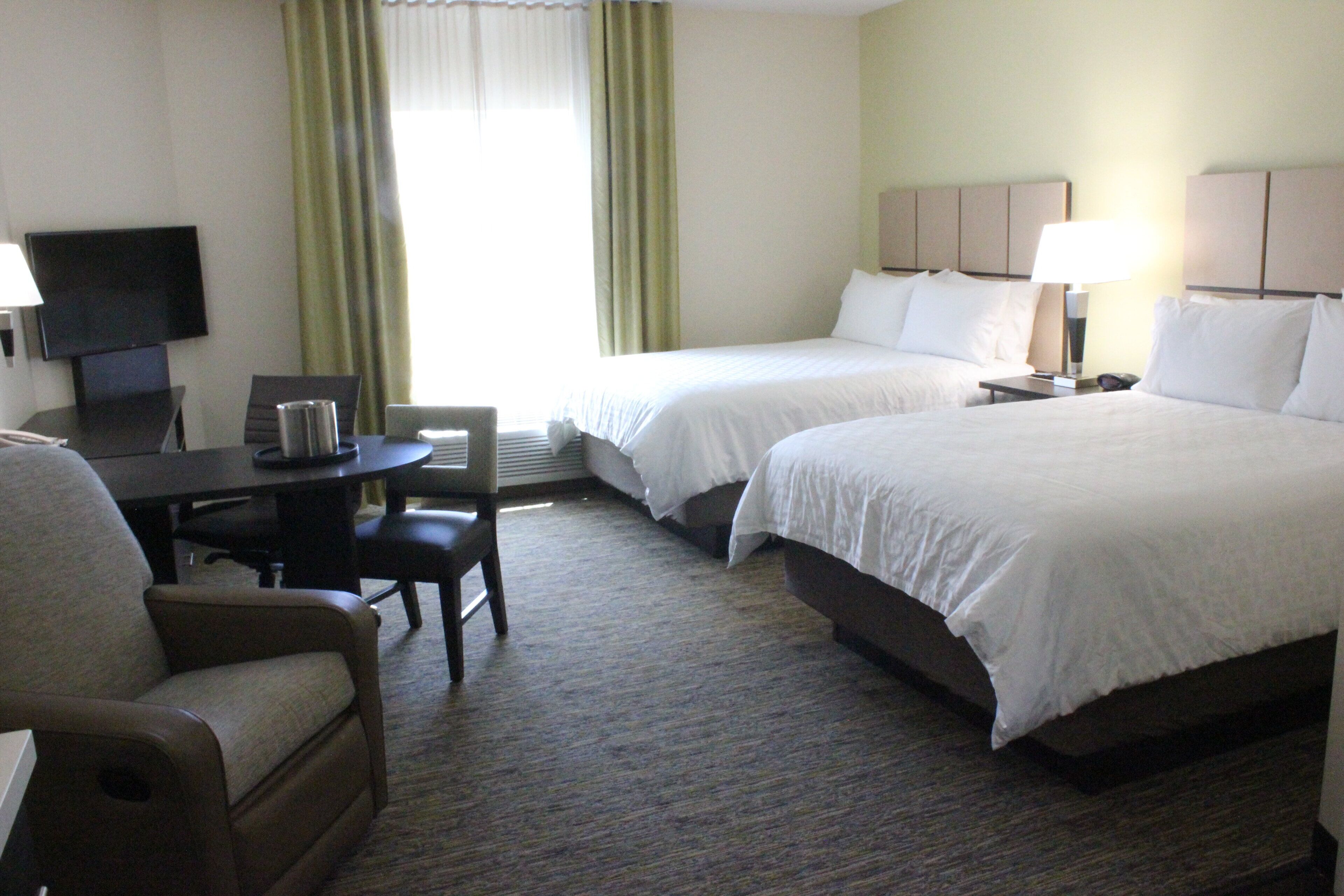 A hotel room with two beds, a desk, a chair, a television, and a window with curtains.