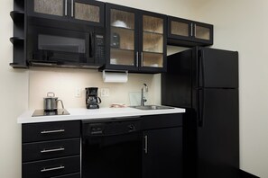 A kitchen with black cabinets, a stainless steel refrigerator, a coffee maker, and a sink. - Candlewood Suites Valdosta Mall by IHG (Valdosta)