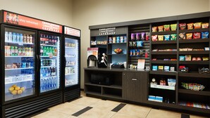 Un refrigerador para bebidas con Coca-Cola y otras bebidas, un microondas y un estante con snacks de diferentes marcas.