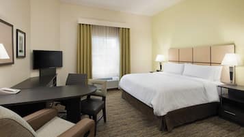 Quarto de hotel com cama, escrivaninha, cadeira, televisão e janela com cortinas.