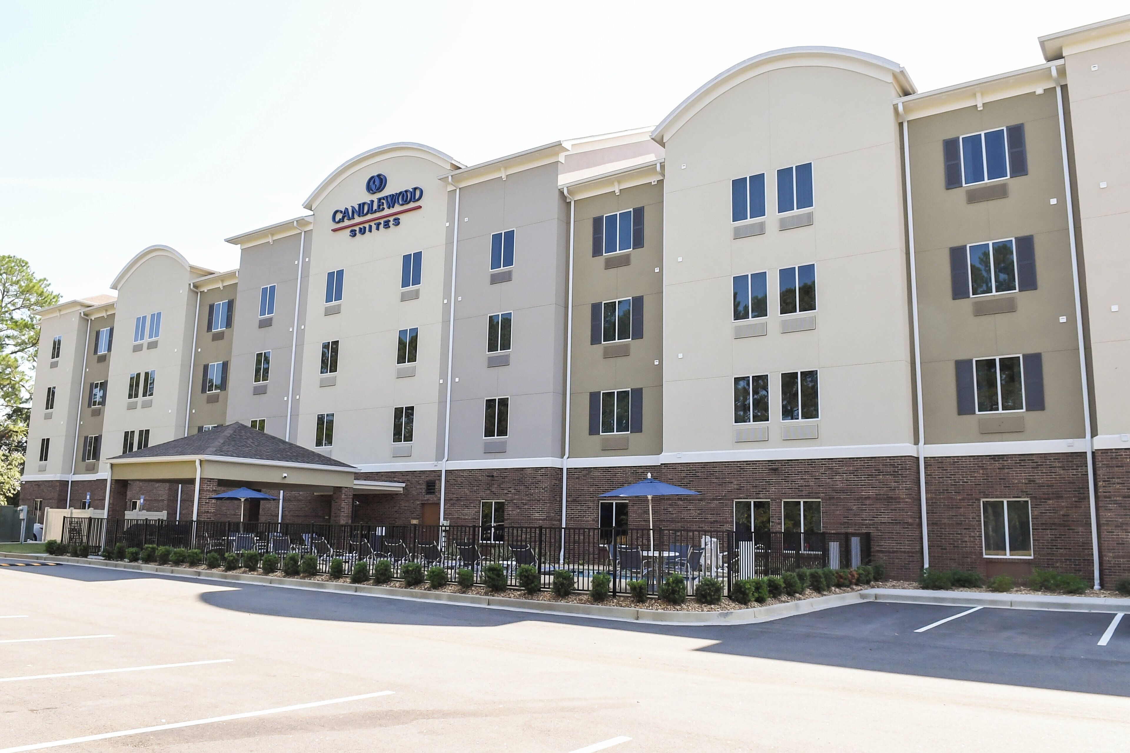 Um hotel com vários andares, com uma placa chamativa da "Candlewood Suites", área de estar externa e estacionamento.