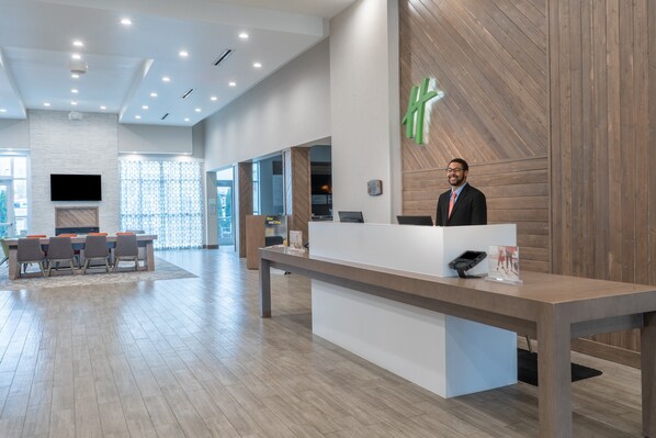 A modern hotel reception area with a wooden reception desk, a flat-screen TV, and a large window with a view of the outside. - Holiday Inn & Suites Memphis Southeast-Germantown by IHG (Memphis)