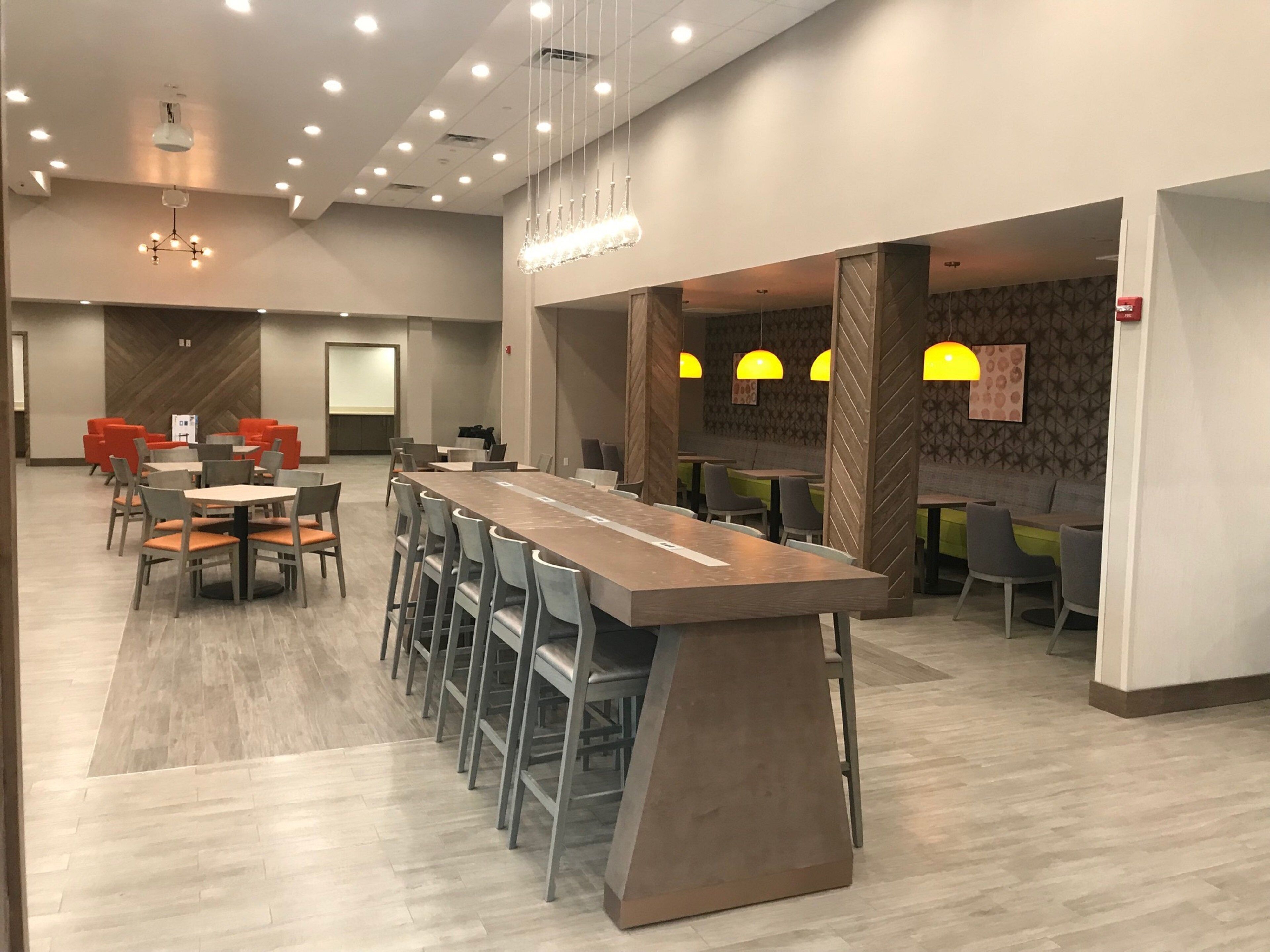 A modern dining area with a long communal table, bar stools, and individual tables.