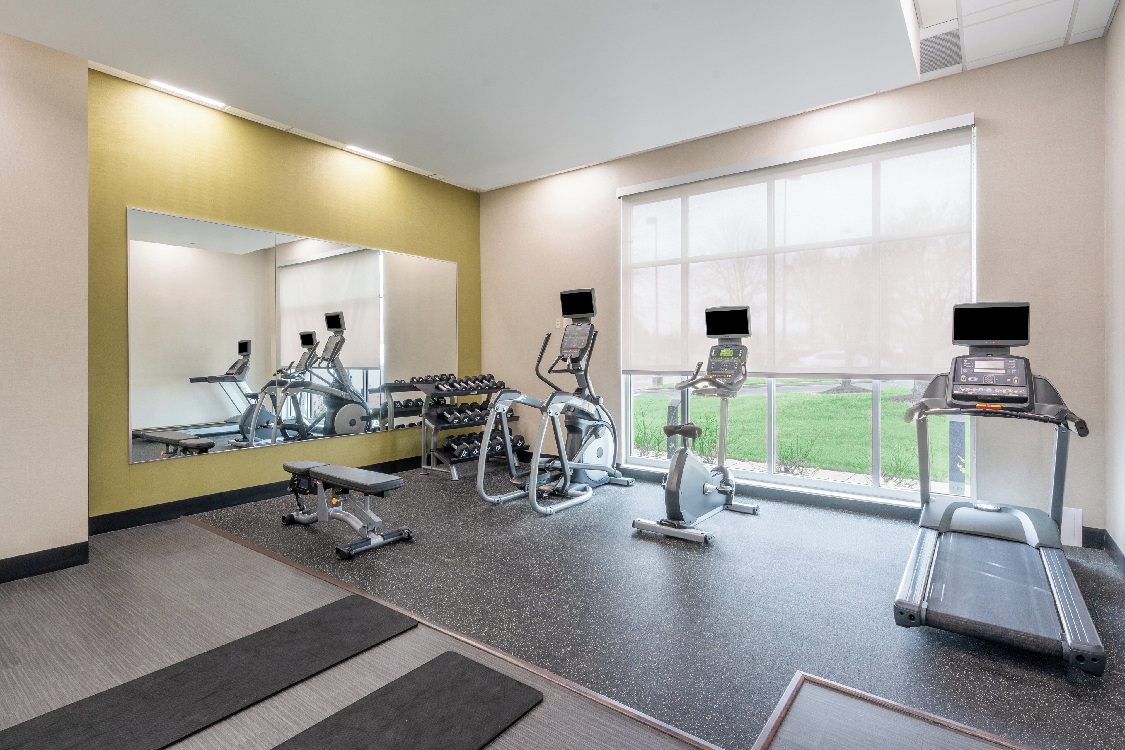 A gym with exercise equipment, a mirror, and a window with a view of the outdoors.