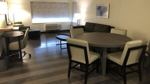 A modern living room with a round dining table, six chairs, a sofa, a coffee table, and a large window with blinds. - Holiday Inn & Suites Memphis Southeast-Germantown by IHG (Memphis)