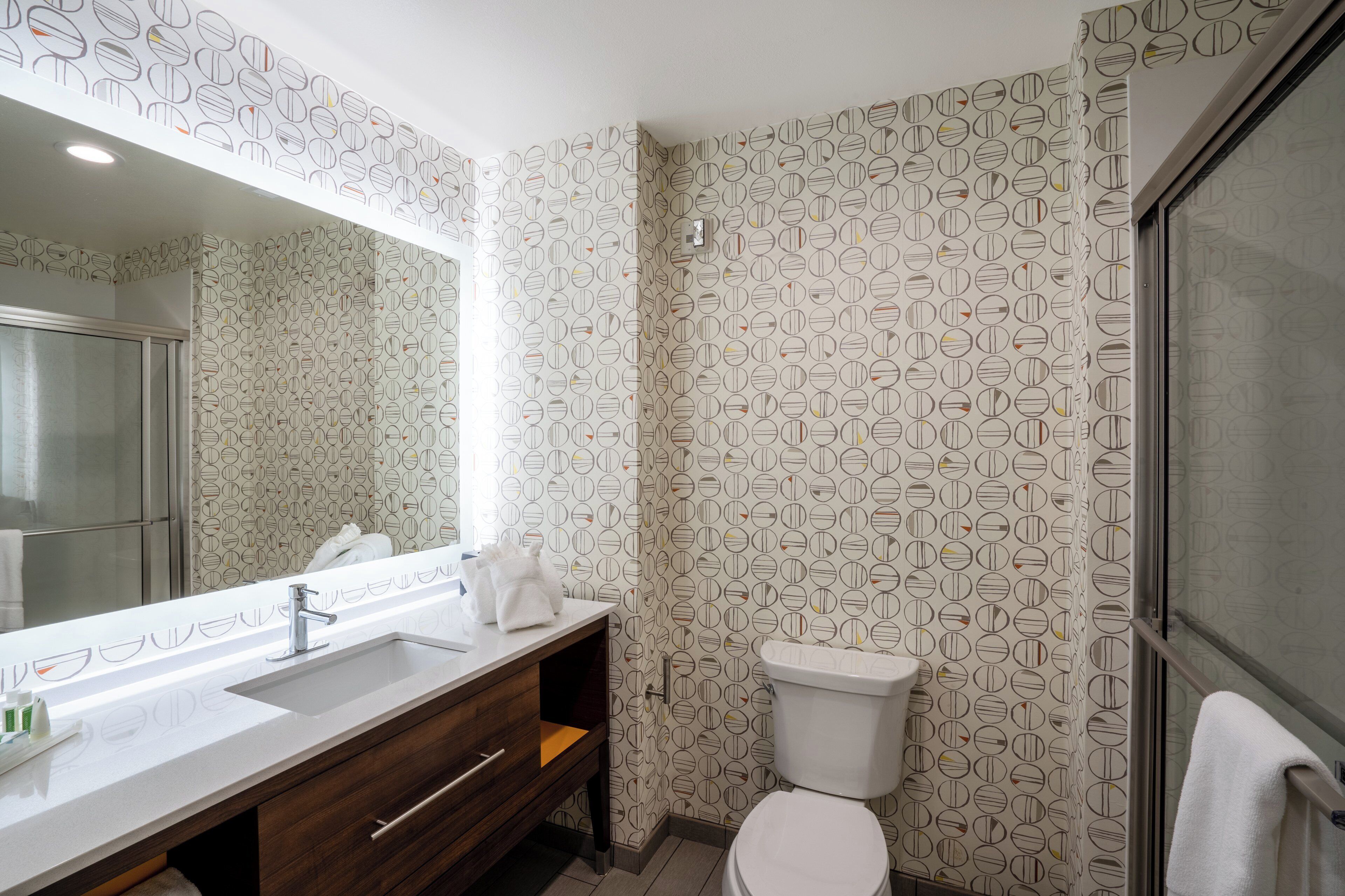 Een badkamer met een modern design, met een grote spiegel, een wastafel, toilet en douche.