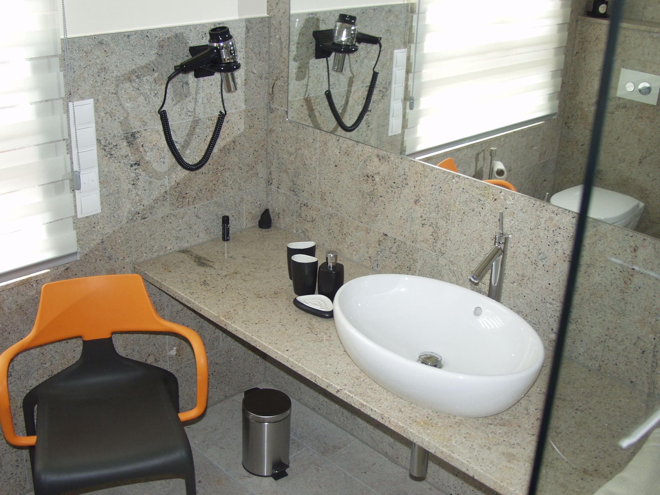 Une salle de bain avec un lavabo blanc, un miroir, un sèche-cheveux et une poubelle.