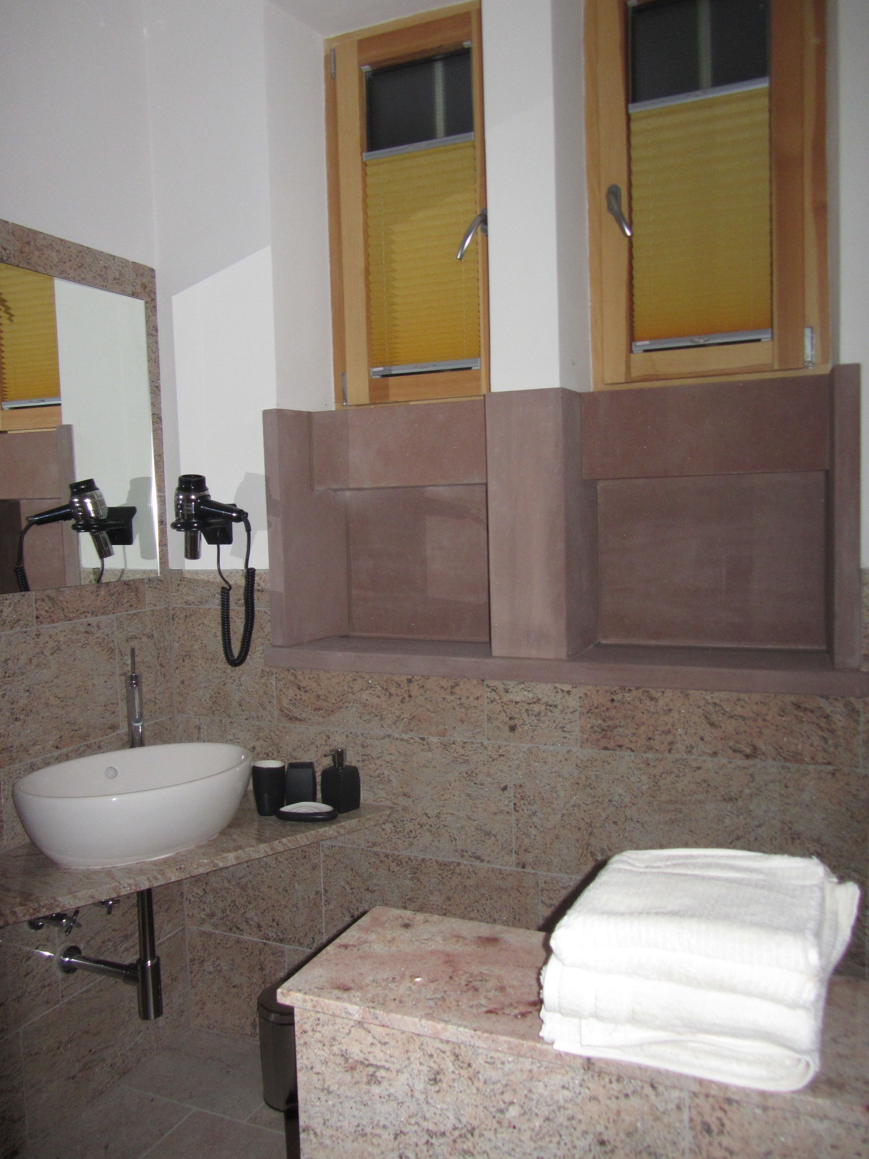 A bathroom with a white sink, a mirror, a towel rack, and a window with blinds.