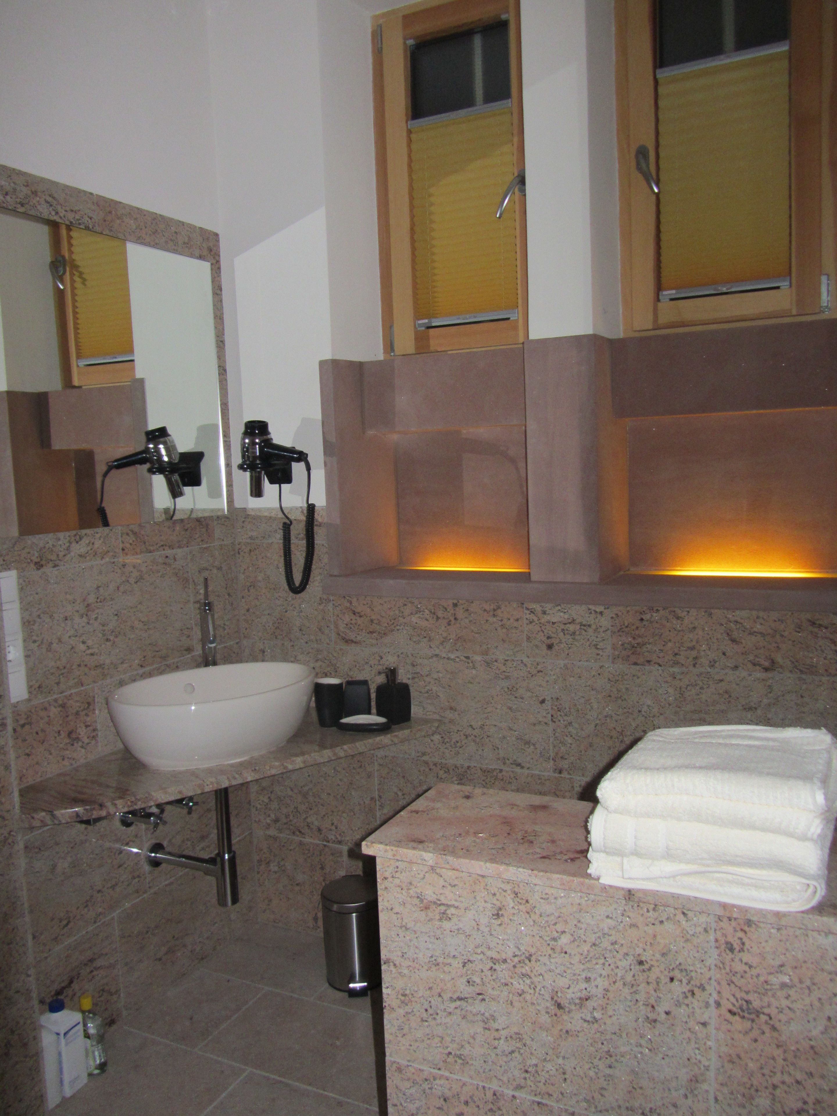 Un baño con lavamanos, espejo, toallero y ventana con persianas.