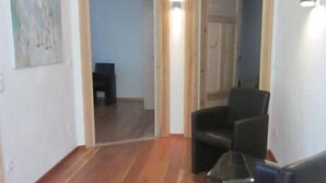 Ein Wohnzimmer mit Holzboden, einer schwarzen Couch, einem Glastisch und einem Bild an der Wand.