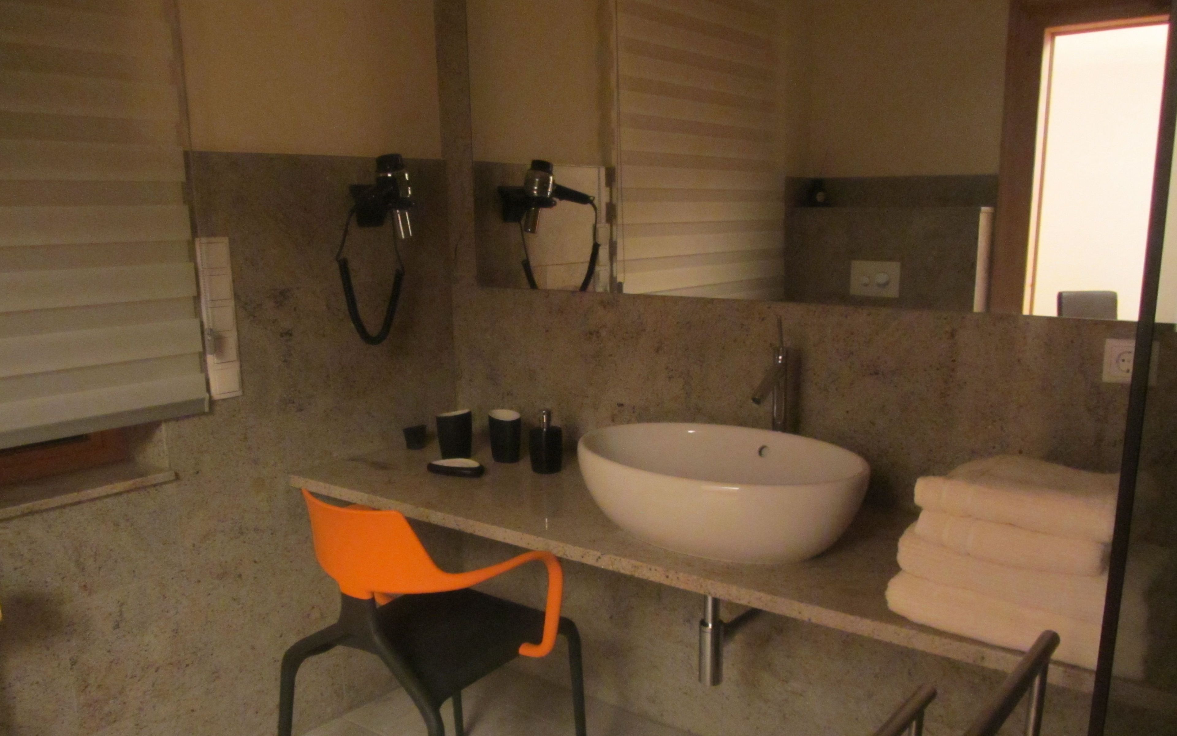 A bathroom with a white sink, a mirror, a towel rack, and a chair.