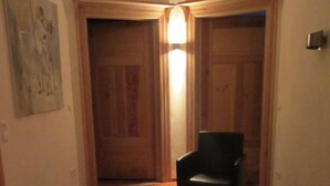 Ein Flur mit Holzboden, einem schwarzen Stuhl und einer Tür mit einer Leuchte.
