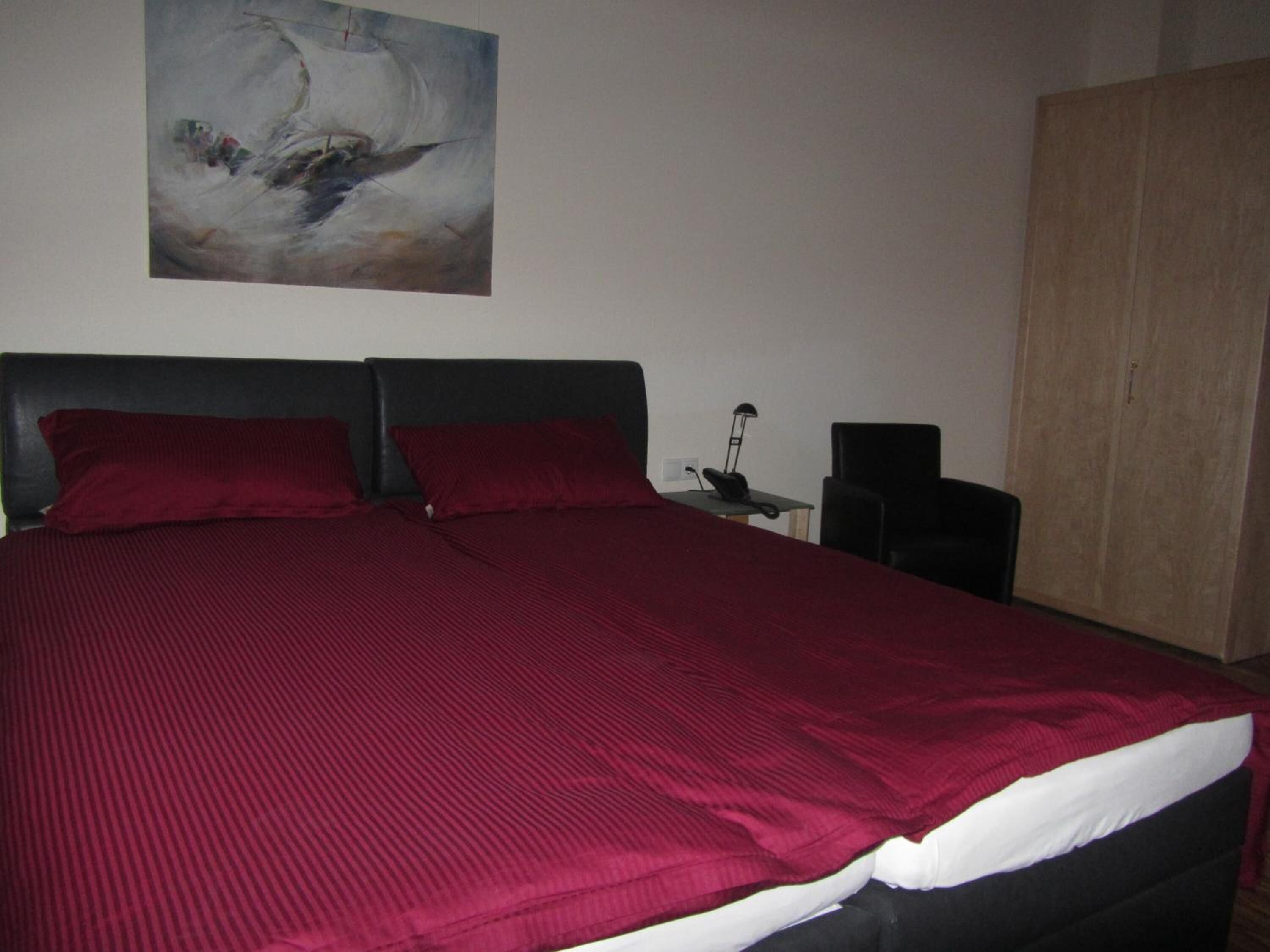 Una camera da letto con un letto grande, due cuscini rossi, una testiera scura, un armadio in legno e un quadro appeso al muro.