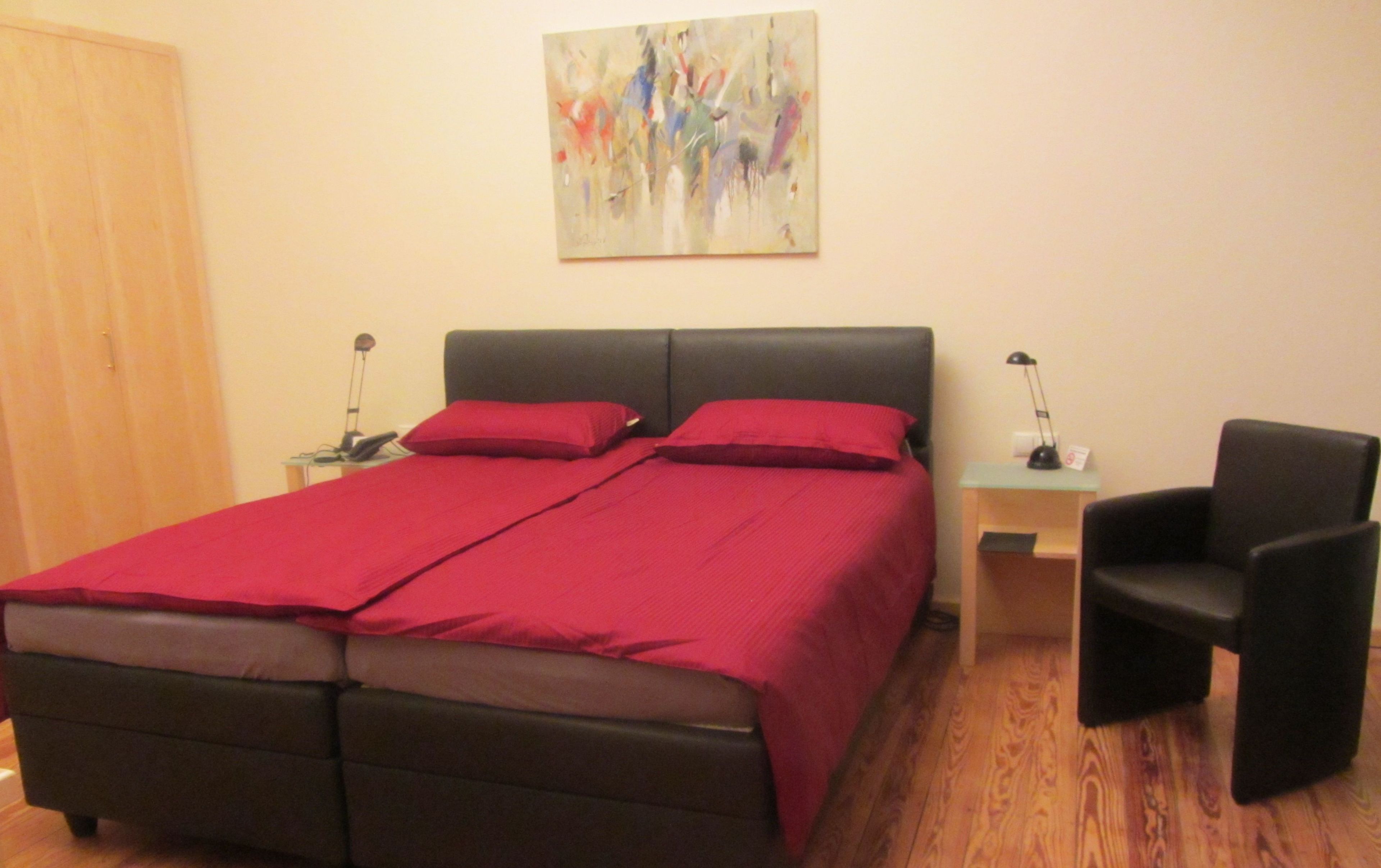 Un dormitorio ordenado con una cama, dos mesitas de noche, una silla y un cuadro en la pared.