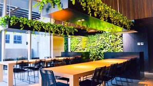 A modern conference room with a long table and chairs, surrounded by lush green plants and a wooden accent wall. - The Escape in Southern Cross Station (Melbourne)