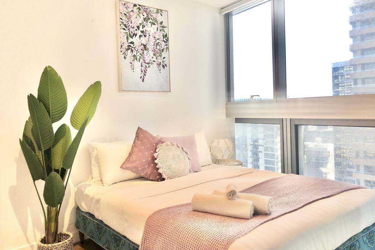 A modern bedroom with a large window, a bed with a pink blanket, and a potted plant.