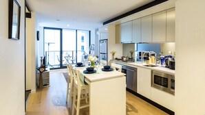 A modern kitchen with white cabinetry, a central island, and a dining area with a table and chairs. - The Escape in Southern Cross Station (Melbourne)