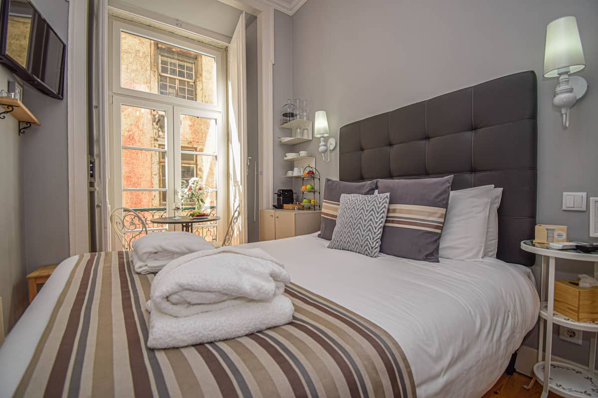 Ein ordentlich gemachtes Bett mit gestreifter Bettwäsche und Handtüchern, ein grauer möbelbezogener Kopfseitenverkleidung und ein Nachttisch mit einer Lampe.