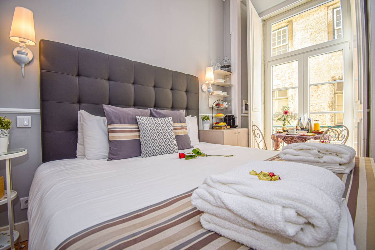 Ein ordentlich bezogenes Bett mit Streifenmuster, ein grauer möbelbezogener Kopfteil und ein Nachttisch mit Lampe.