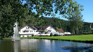 A hotel with a restaurant and a fountain by a lake. - Hotel Pappelhof (Weidenbach)