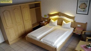 A hotel room with a large bed, wooden wardrobe, bedside tables, and a small table with a vase. - Hotel Pappelhof (Weidenbach)