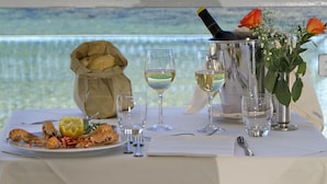 A table set with a seafood dish, wine glasses, a bottle of champagne, and a vase with flowers, overlooking a beach. - Hotel La Playa (Pollica)
