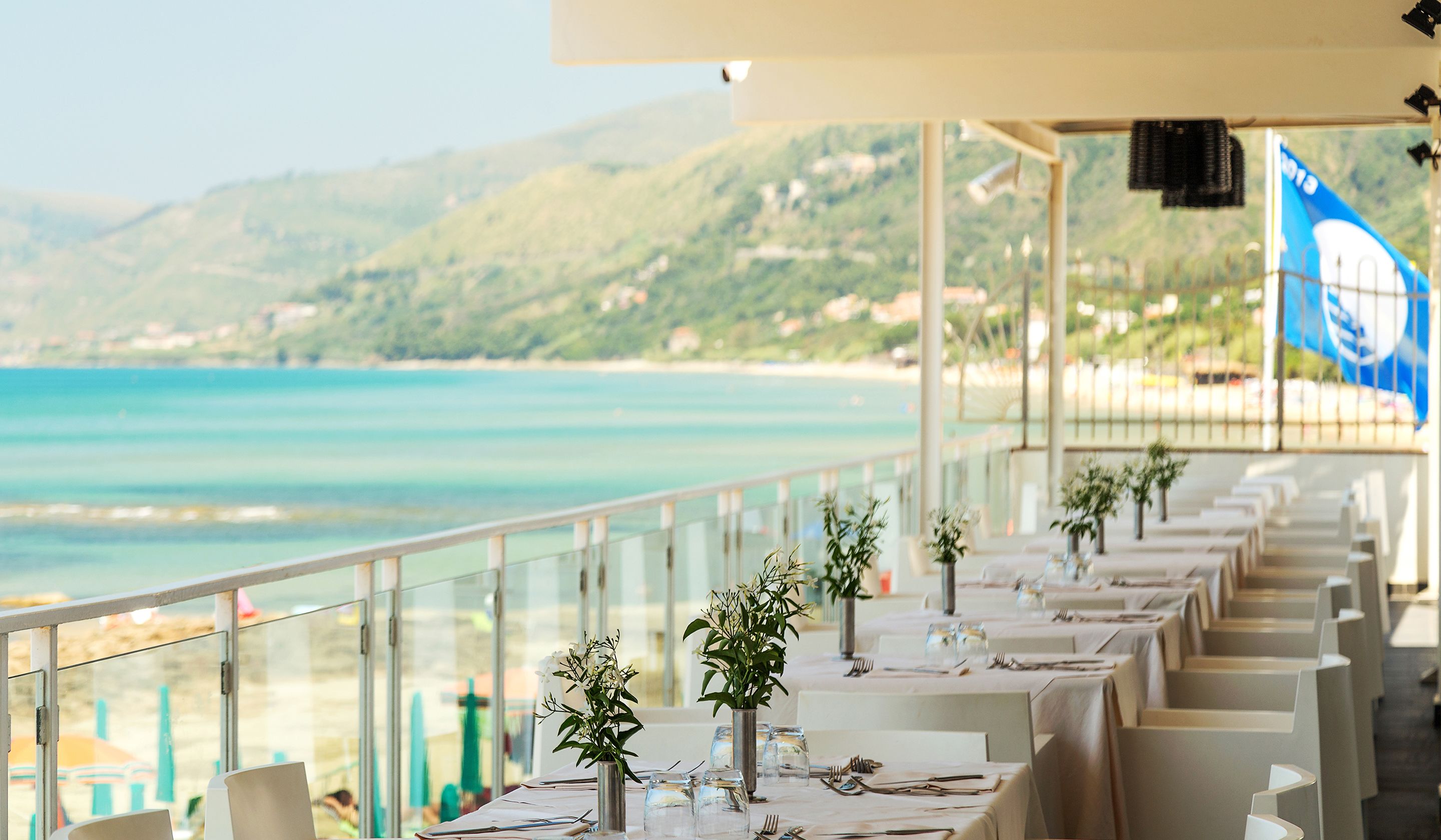 Un restaurant en bord de mer, avec des tables dressées pour le dîner, offrant une vue sur la plage et la mer.