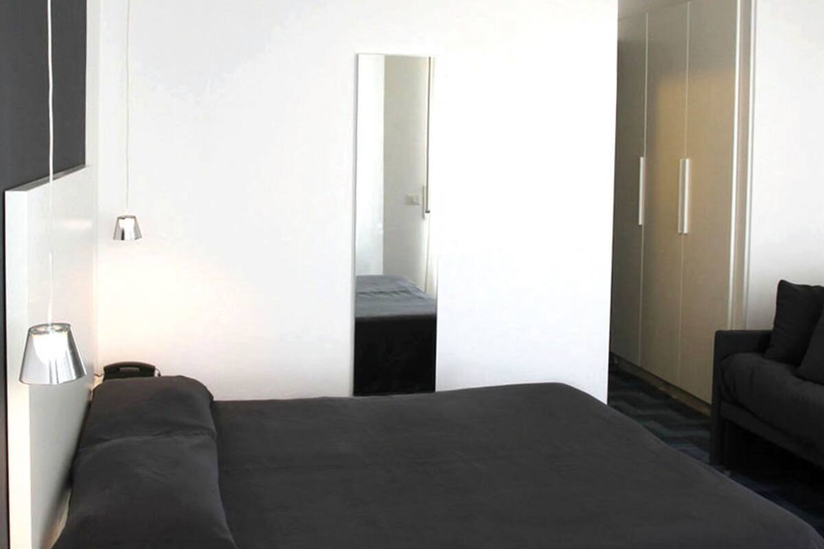 A modern hotel room with a bed, a sofa, a mirror, and a wardrobe.
