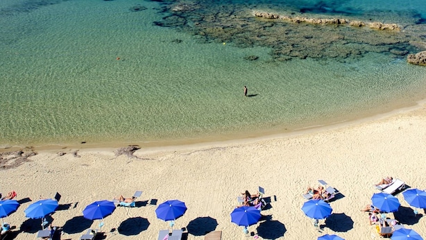 A beach with clear turquoise water, a sandy shore, and several blue umbrellas providing shade. - Hotel La Playa (Pollica)