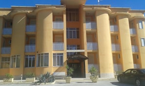 Un edificio de varios pisos con balcones, una entrada central y plantas en macetas.