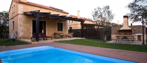 A stone building with a pool, outdoor seating, and a barbecue area.