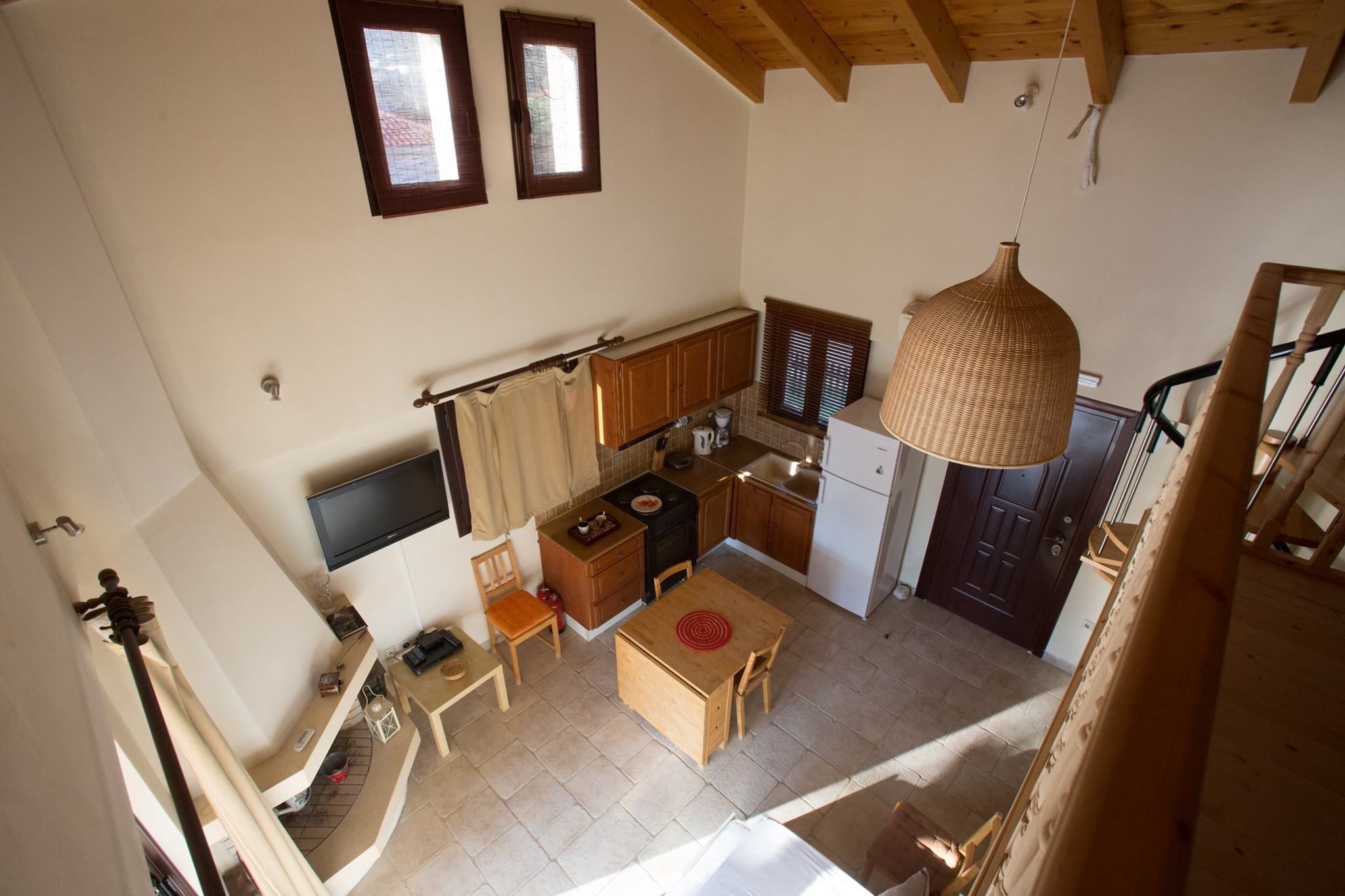 A compact kitchen with wooden cabinets, a dining table, and a hanging light fixture.