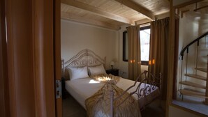Ein Schlafzimmer mit Holzboden, einem Bett mit dekorativer Kopfteil, einem Nachttisch und einer Treppe rechts.