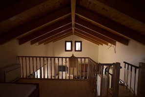 A high-ceilinged attic room with a wooden staircase, a bed, and a small window.