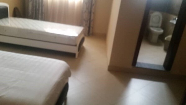 A room with a bed, a small table, and a mirror reflecting a toilet.