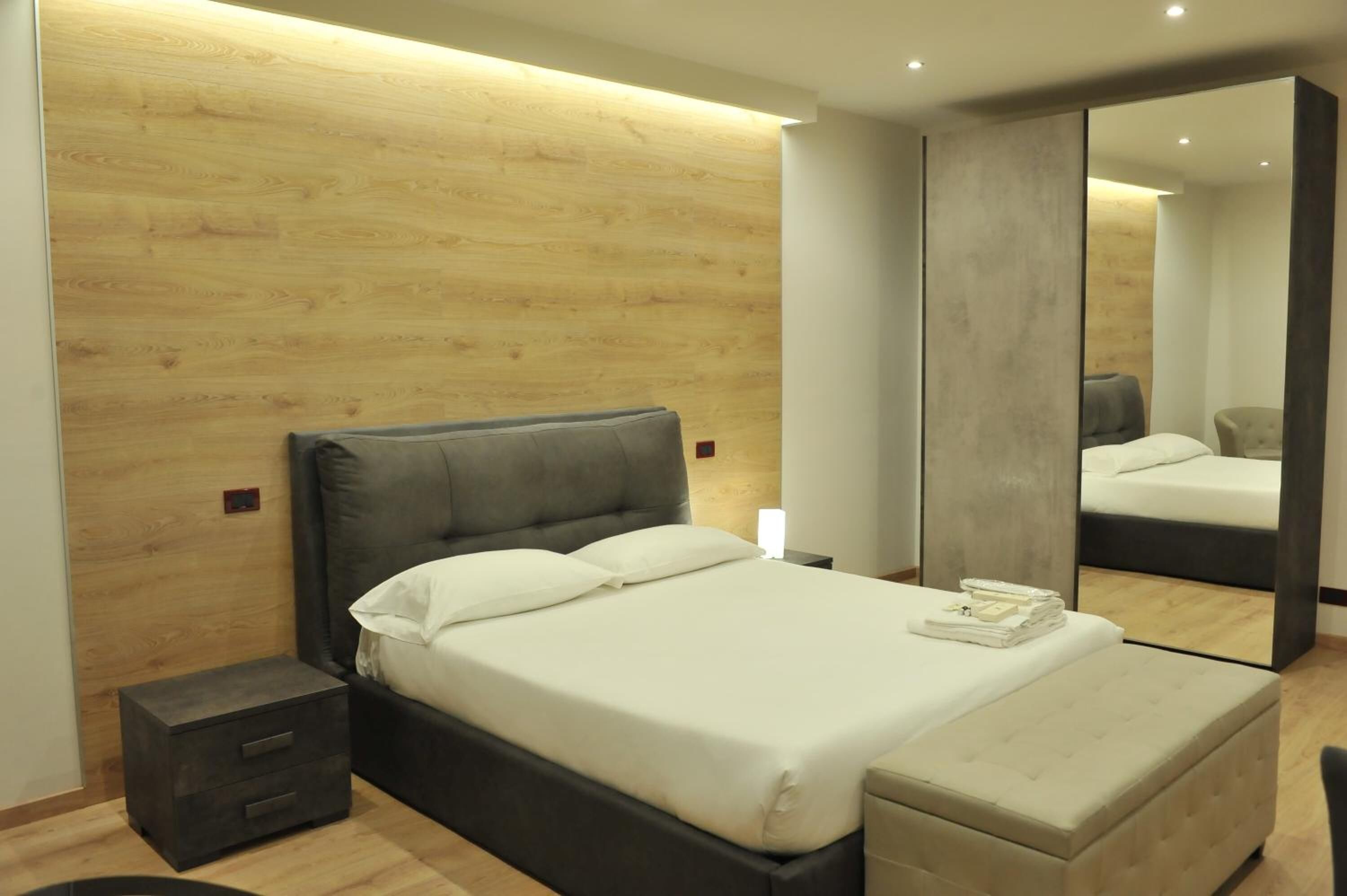 Ein modernes Schlafzimmer mit Holzvertäfelung, einem großen Bett mit weißer Bettwäsche, einem Nachttisch und einem Spiegel.
