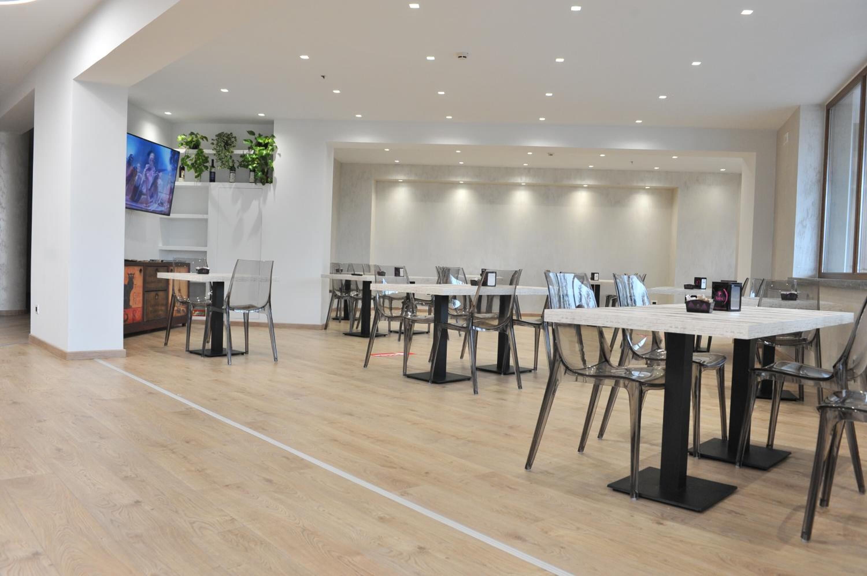 A modern dining area with multiple tables and chairs, a flat-screen TV mounted on the wall, and a plant shelf.
