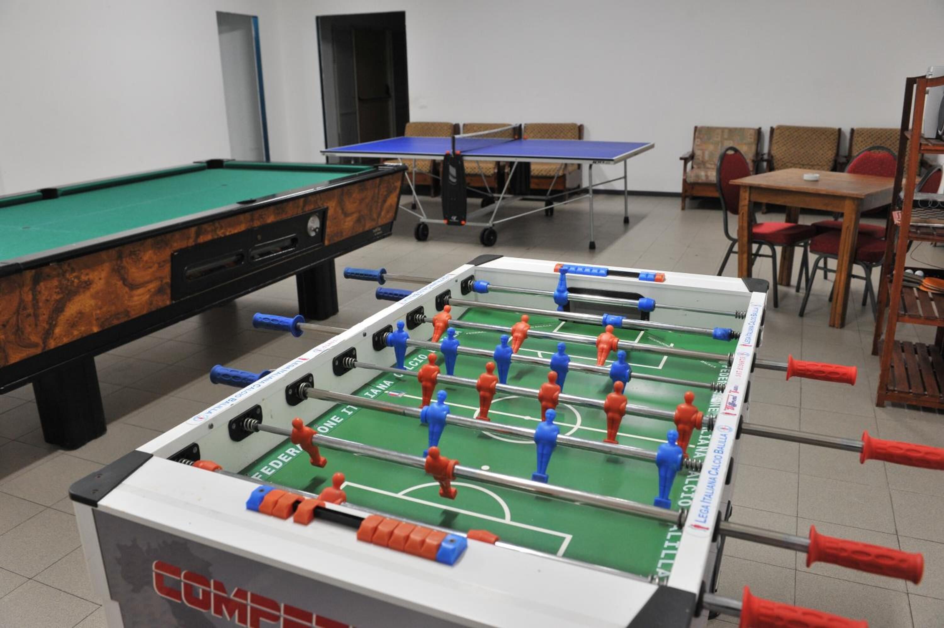 A room with a foosball table, a pool table, and a ping pong table.