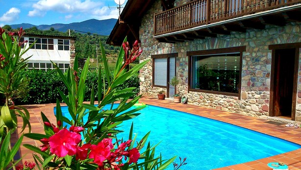 Un bâtiment en pierre doté d’une piscine, entouré de verdure et avec des montagnes en arrière-plan.