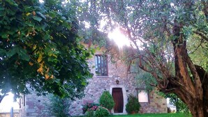 Un bâtiment en pierre avec une porte centrale, entouré d’une pelouse bien entretenue et de divers arbustes.