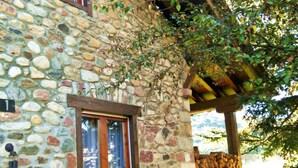 Un bâtiment en pierre avec une pergola en bois, une fenêtre et une pile de bois de chauffage.