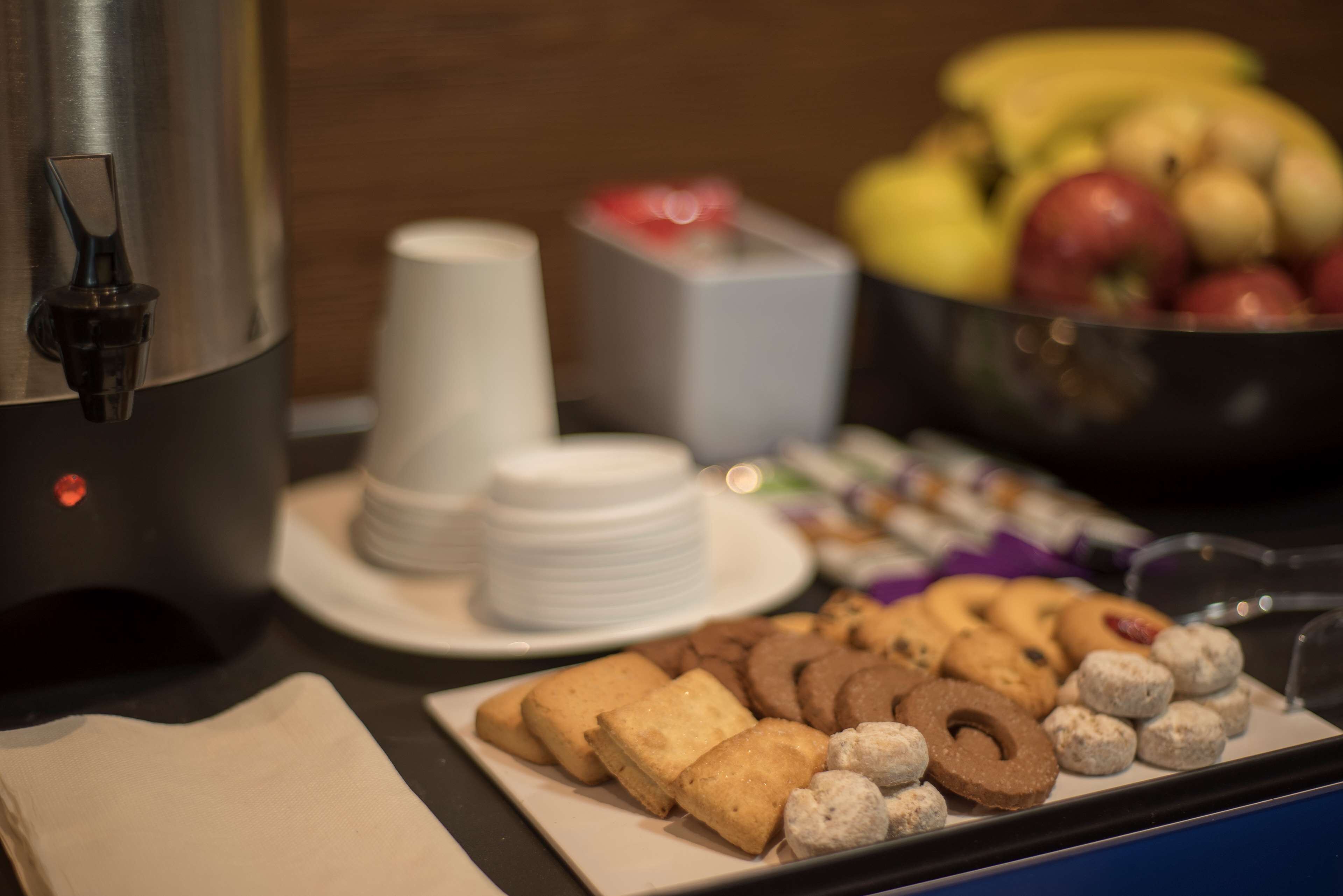 Una mesa de buffet con diversos alimentos, incluyendo galletas y pasteles, y un cuenco de fruta al fondo.