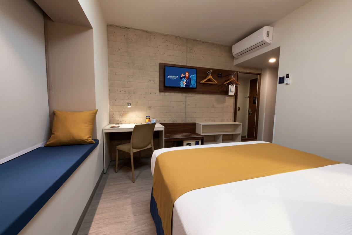 A hotel room with a bed, a desk, a chair, a TV, and a wardrobe.