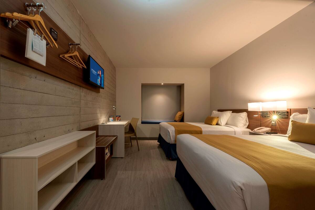 A hotel room with two beds, a desk, and a TV mounted on the wall.