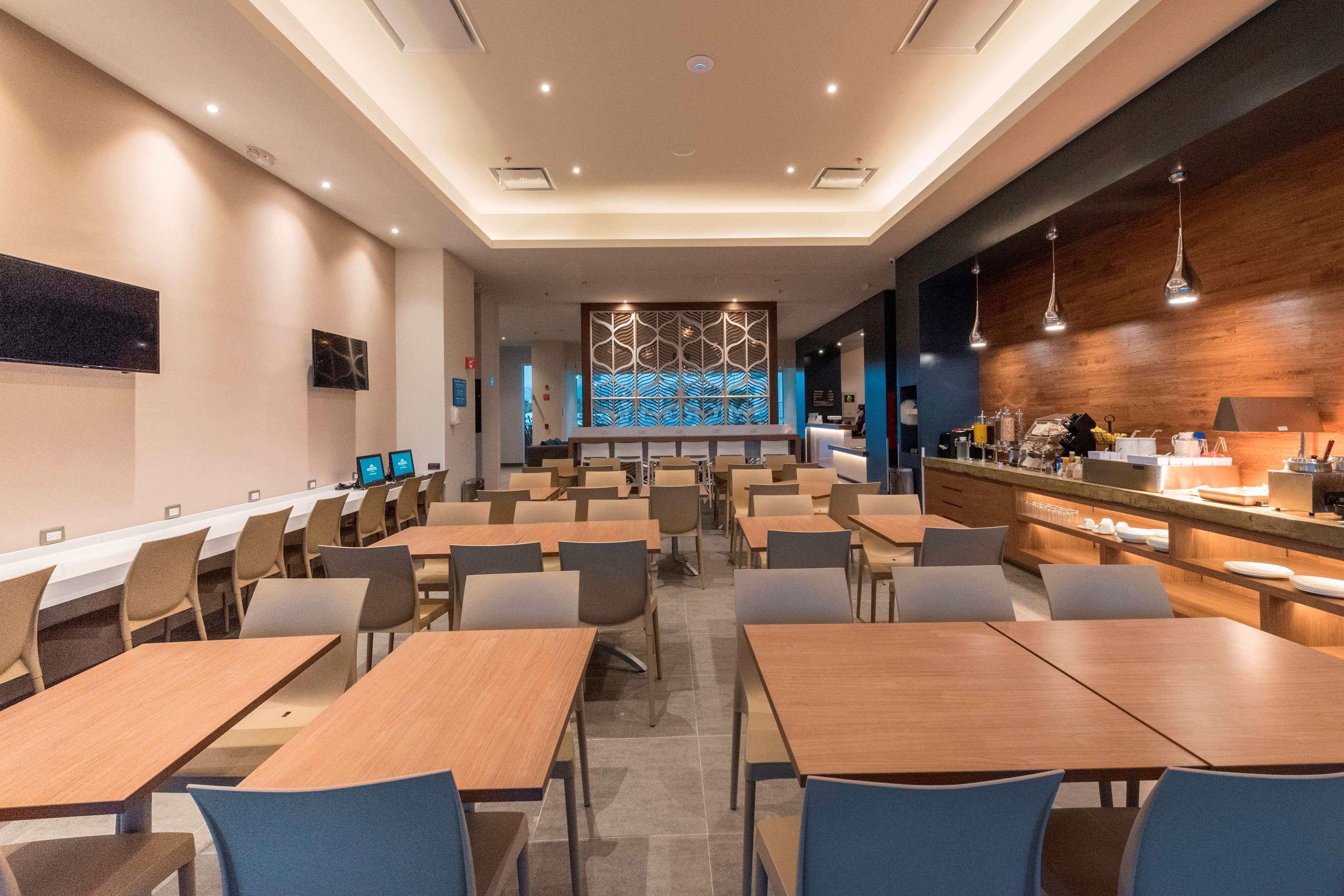 A modern hotel lobby with a long reception desk, multiple seating areas, and a decorative wall with a geometric pattern.