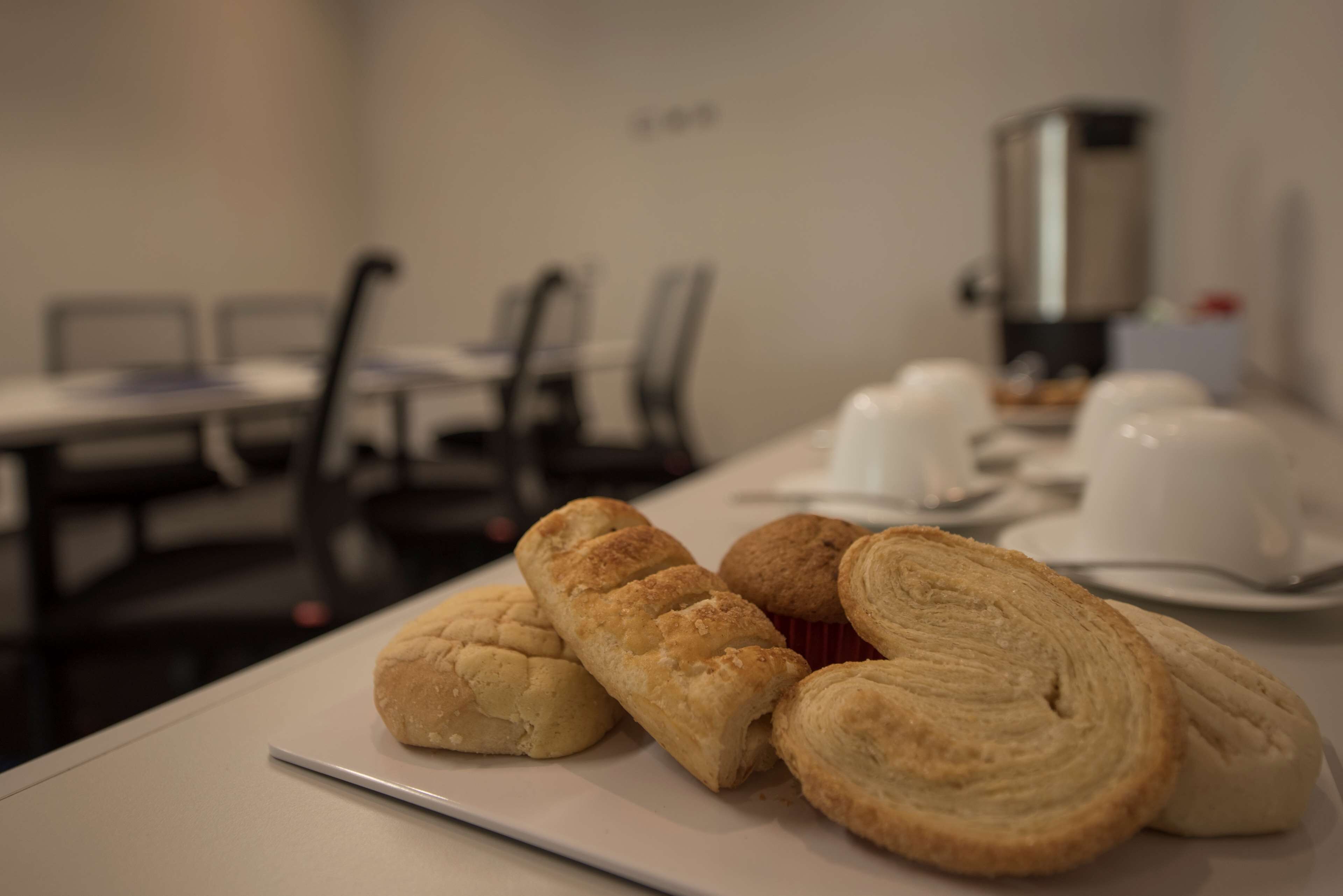 A table with pastries and a coffee machine in a room with chairs and tables.