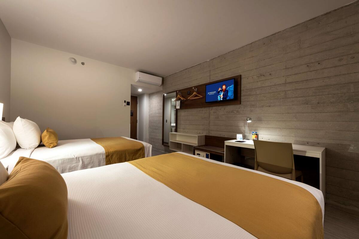 A hotel room with two beds, a desk, a chair, a television, and a wardrobe.
