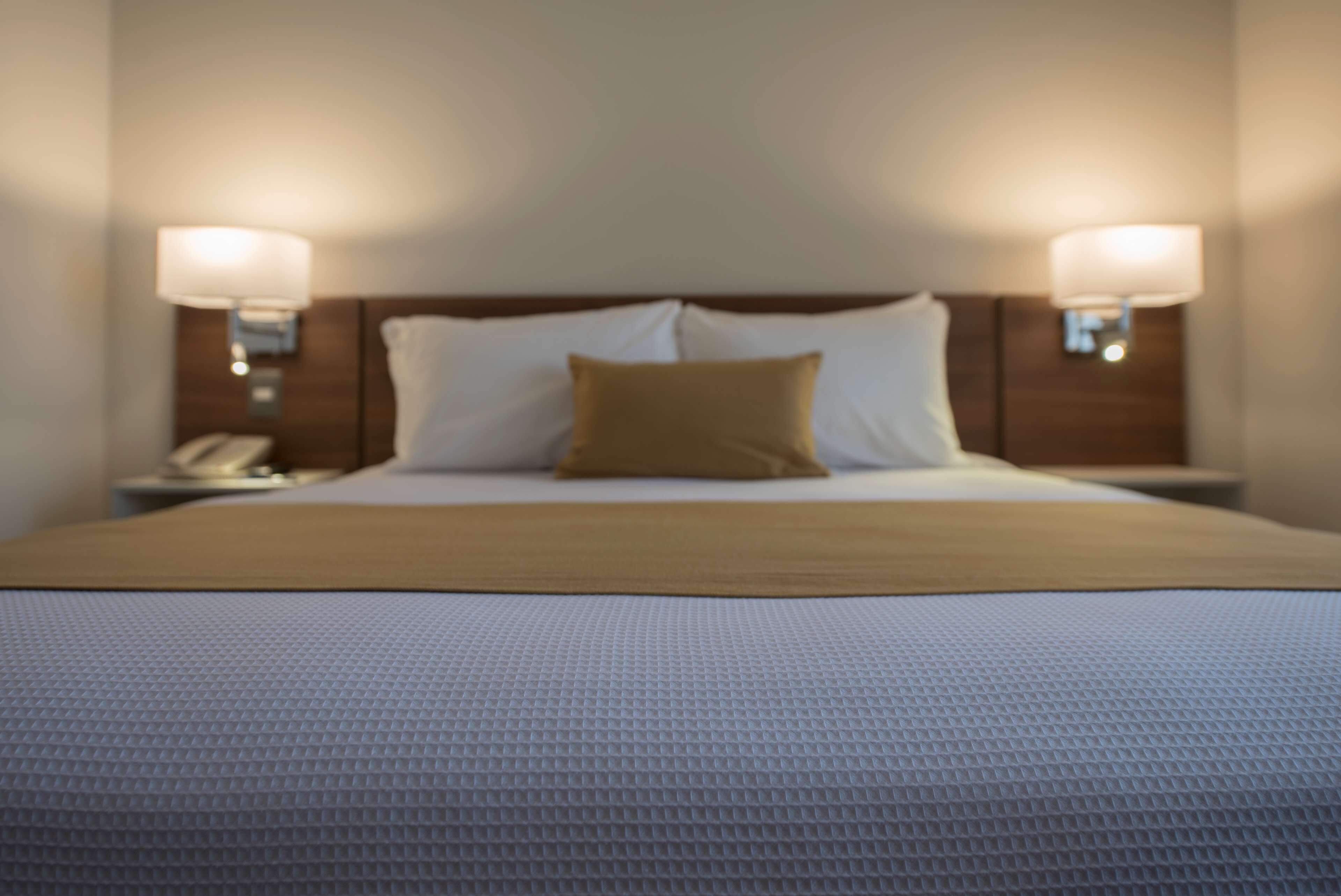 A neatly made bed with a white and beige duvet, two bedside lamps, and a nightstand with a telephone.