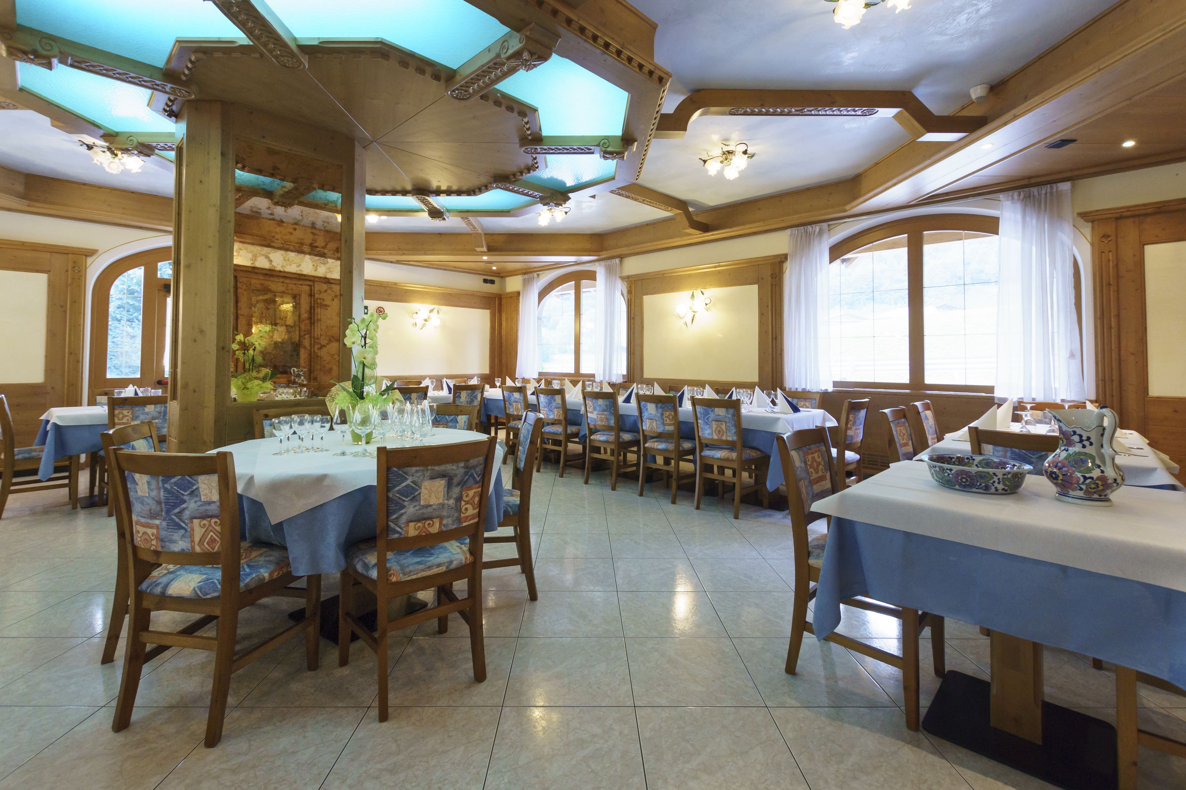 A dining area with multiple tables and chairs, wooden beams on the ceiling, and large windows allowing natural light.