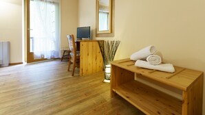 Ein Zimmer mit Holzboden, einem Schreibtisch mit Computer, einem Spiegel und einer Bank mit Handtüchern.